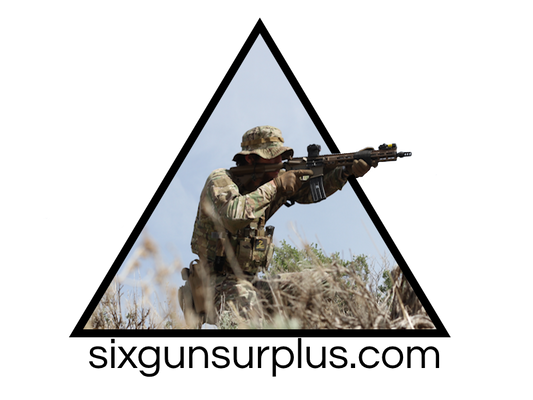 A soldier in camouflage uniform and helmet, crouching in a grassy field and aiming a rifle, framed within the logo of Six Gun Surplus. The background features a clear sky with scattered bushes. This scene encapsulates the essence of the Six Gun Surplus Gift Card from Six Gun Surplus.