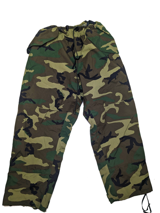 A pair of U.S. Issue ECWCS Woodland Gore-Tex Pants from Six Gun Surplus, designed with a drawstring waist and crafted from military-grade materials. These pants feature a green, brown, beige, and black camouflage pattern typical of military styles. They are laid out flat against a solid black background, highlighting their rugged texture.